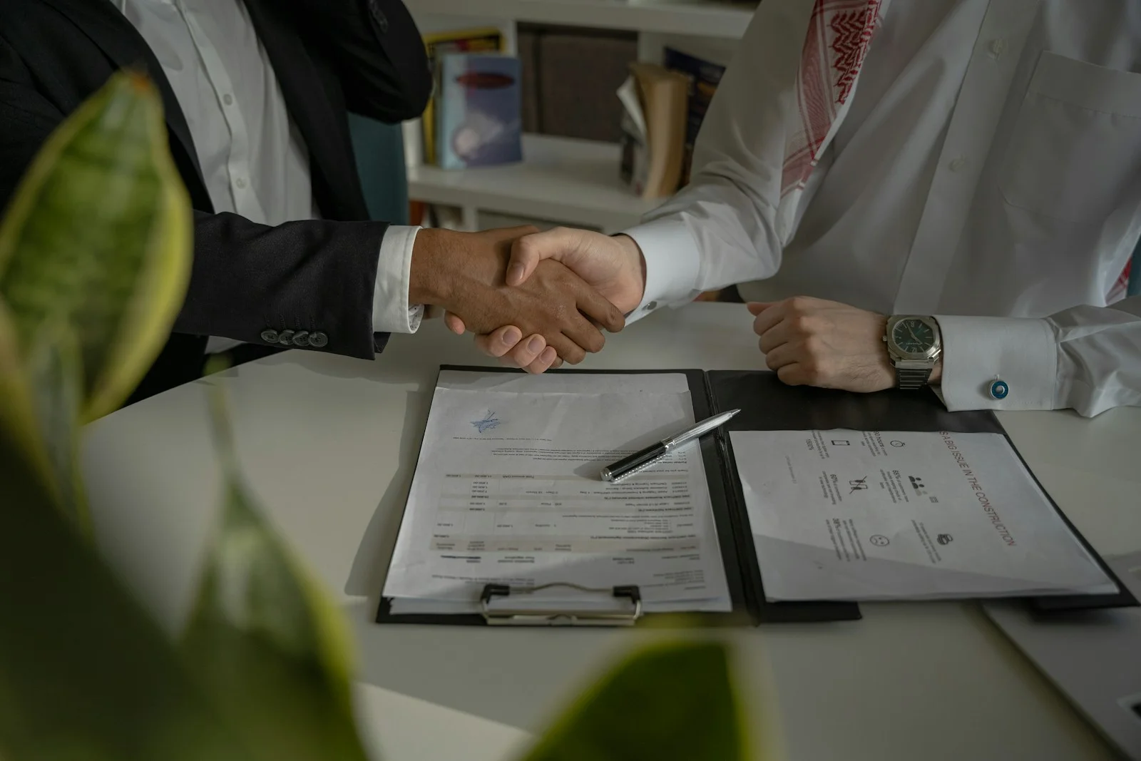 Two people shaking hands over a contract on a table