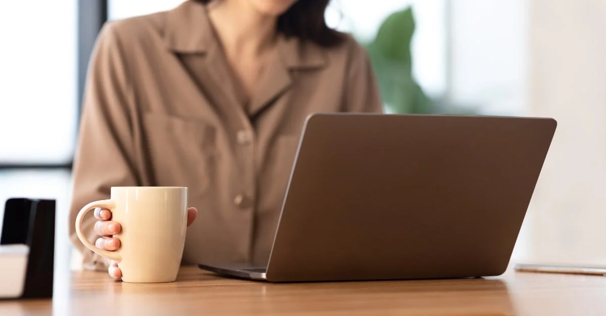 Woman holding a cup of coffee in front of her laptop